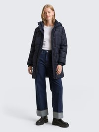 Tmavě modrý prošívaný kabát s kapucí, se zipem, prošívanou strukturou a elastickými manžetami. Kombinován s tmavě modrými džínami a černými kozačkami.