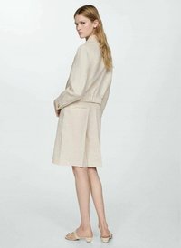 Beige linnejacka med elastisk midja och två sidofickor, i kombination med en matchande kjol med veckdesign. Enkla sandaler fulländar looken.