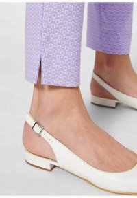 Witte slingback schoenen met een platte hak hebben een gladde leren afwerking en een zilveren gesp, in combinatie met lichtlila gemusterde cropped broeken.