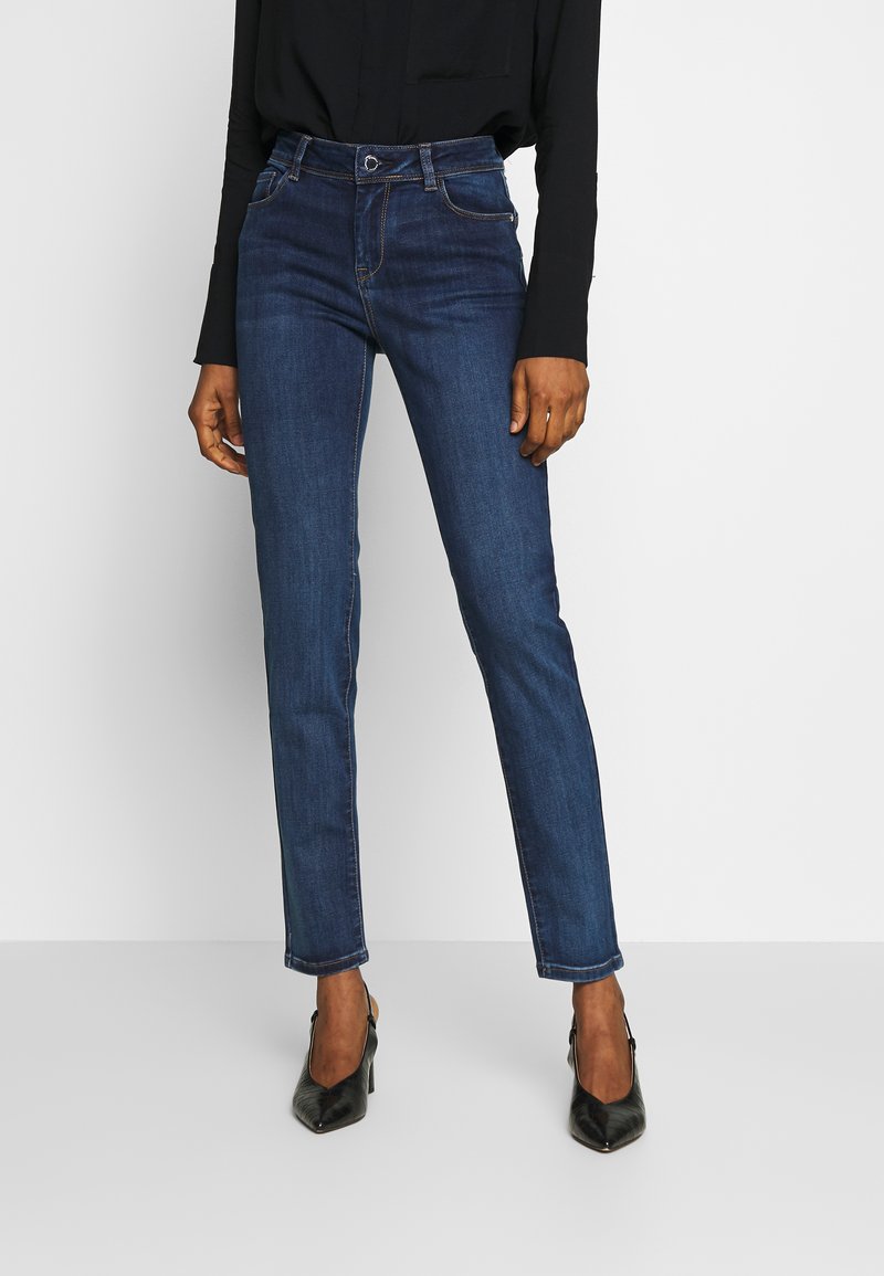 Pantalones vaqueros de mezclilla azul oscuro con un diseño ajustado, que cuentan con cinco bolsillos, una cintura con trabillas para el cinturón y sutiles detalles de costura.