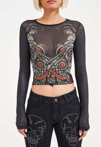 Long-sleeve mesh crop top with colorful graphic print, featuring a fitted design. Paired with high-waisted black jeans embellished with skull details.