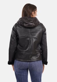 Giacca di pelle nera con finitura testurizzata, dotata di un cappuccio imbottito e trapuntato e dettagli in pelliccia sintetica ai polsini. La vista posteriore mostra cuciture sartoriali.