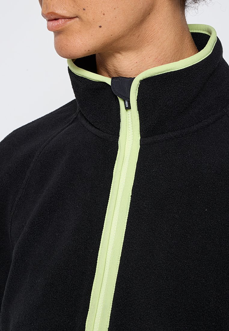 Schwarze Fleecejacke mit hohem Kragen, ausgestattet mit einem kontrastierenden, limettengrünen Reißverschluss. Weiche Textur, minimalistisches Design und keine zusätzlichen Muster.