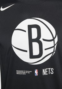 Schwarz sportliches T-Shirt mit einer großen weißen Basketballgrafik und dem Text 'B' und 'NETS'. Enthält den Hinweis 'Nach genauen Spezifikationen entwickelt'.