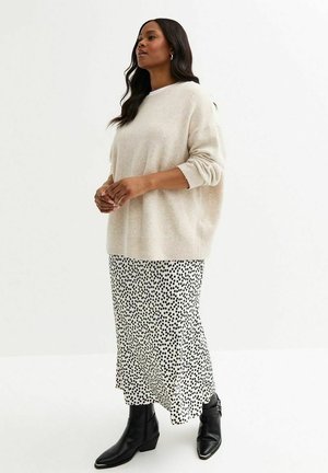 Beige, överdimensionerad stickad tröja med rullkantar, i kombination med en svart och vit prickig midikjol och svarta ankelstövlar.