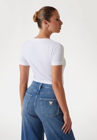 T-shirt bianco a maniche corte abbinato a jeans in denim blu a vita alta con una toppa a forma di triangolo e due tasche posteriori.