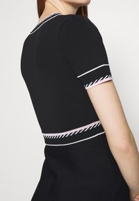 Abito nero con maniche corte, caratterizzato da accenti a righe bianche e rosa sul collo e sulle maniche. La texture a coste è visibile.
