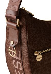 Bolso de hombro marrón texturizado con cremallera dorada, detalles en cuero marrón y una correa de hombro con estampado y detalle de logo.