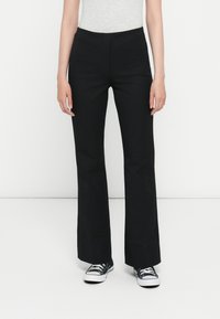 Black flared pants made of smooth fabric, featuring a mid-rise waist and a straight fit through the legs, paired with black sneakers.