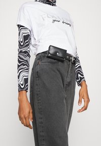 Camiseta blanca con el texto "SIGUE tus sueños", mangas largas negras con estampado, jeans gris de cintura alta y una bolsa de cinturón negra.