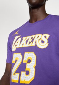 Ljubičasti pamučni majica s žutim natpisom "LAKERS" i perforiranim bijelim "23" na prednjoj strani, s malim narančastim Jumpman logom blizu ovratnika.