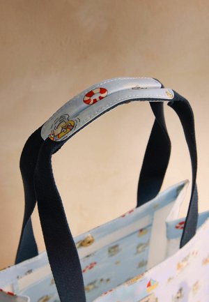 Niebieska torba na ramię z uchwytami z ciemnoniebieskiej tkaniny oraz osłoną na rączkę ozdobioną czerwonymi i białymi ilustracjami koła ratunkowego i łodzi.