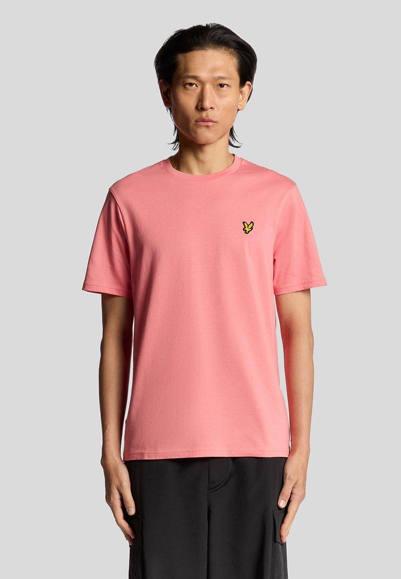 T-shirt di cotone rosa con scollatura rotonda e maniche corte, con un piccolo logo di una farfalla gialla sul lato sinistro del petto.