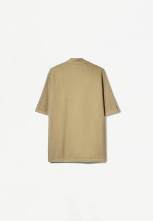 Chemise beige à manches courtes avec un col, présentant un tissu texturé et un ourlet droit, vue de dos sur un fond blanc.