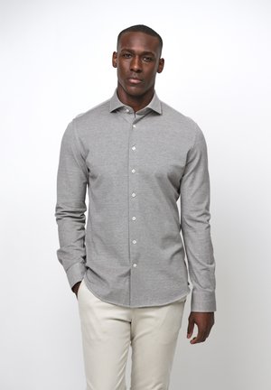 Camisa gris de manga larga con botones y cuello clásico. Hecha de una tela ligera, presenta una textura suave y botones blancos.