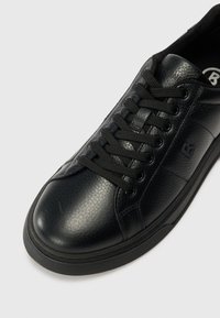 Baskets en cuir noir avec une finition texturée, bout rond, lacets noirs et semelle en caoutchouc. Présente un logo sur le côté.