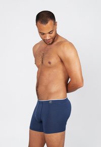 Marineblauwe boxershorts van zachte stof, met een witte tailleband, een foedraal aan de voorkant en een ontwerp tot halverwege de bovenbenen.