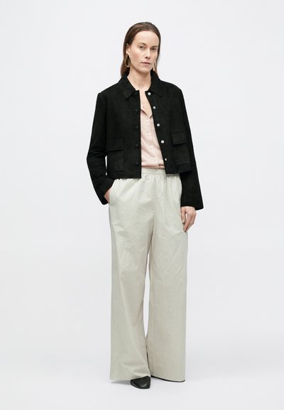 Μαύρο σουέτ cropped σακάκι με κλείσιμο με κουμπιά και δύο μπροστινές τσέπες, σε συνδυασμό με ανοιχτό γκρι παντελόνι φαρδιάς γραμμής και ροζ πουκάμισο με κουμπιά.