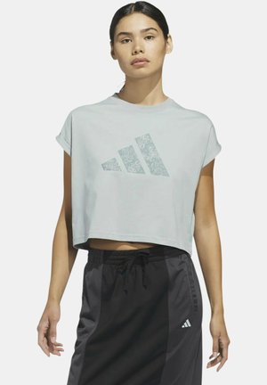 Donna che indossa una T-shirt corta grigio chiaro con logo floreale Adidas e pantaloncini sportivi neri con coulisse e logo Adidas.