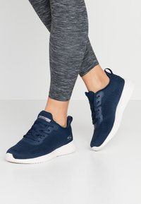 Námornické modré sportovní boty s texturovaným pleteným materiálem, bílé podrážky a tkaničky. Vybavené logem na boku a poutkem na patě.