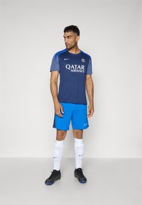 Herre fodboldudstyr bestående af en navyblå og grå trøje med hvid branding og blå shorts. Inkluderer sorte støvler og hvide sokker med accenter.