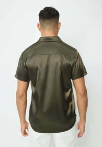 Chandail à manches courtes en satin vert olive foncé. Texture lisse avec un éclat subtil, doté d'un col évasé et d'une couture de empiècement au dos.