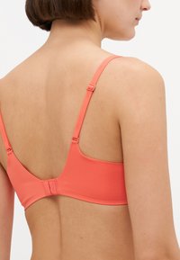 Koraalgekleurde bh met verstelbare bandjes en haaksluiting. Gemaakt van een zachte stof, met een minimalistisch ontwerp en subtiele branding.