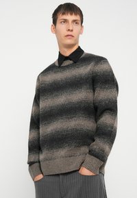 Gray and beige striped sweater with a round neckline and ribbed cuffs, layered over a black collared shirt, featuring a soft texture.