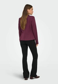Maronfarget blazer med tætsiddende design, bageste sømme og lange ærmer, parret med sorte flagrende bukser og brune blokhælede sko.
