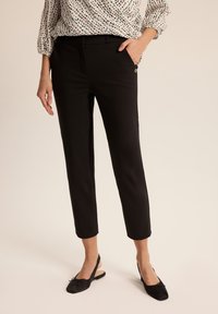 Czarne dopasowane spodnie o kroju slim i skróconej długości. Posiadają pas, kieszenie boczne oraz subtelny metaliczny akcent.