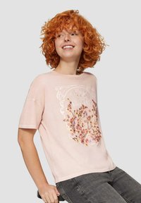 Jasnoróżowa koszulka z krótkim rękawem z kwiatowym nadrukiem w delikatnych kolorach, okrągły dekolt, luźny krój oraz gładka tekstura materiału.