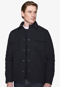 Sort uldjakke med knaplukning, to brystlommer og klassisk krave. Teksturen ser glat og varm ud.