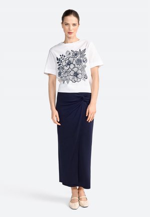 T-shirt bianco in cotone con stampa floreale navy, abbinato a una gonna avvolgente navy di lunghezza al ginocchio con dettaglio torcigliato nella parte anteriore. Ballerine beige.