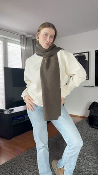Ribbed dark brown scarf worn over a white sweater, paired with light blue jeans. The scarf is long and has a textured appearance.
