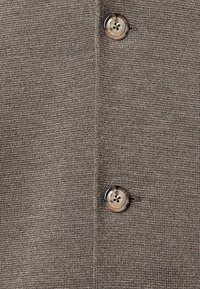 Tessuto a maglia marrone con due bottoni rotondi, uno con quattro fori e testo inciso, che crea un aspetto liscio e testurizzato.