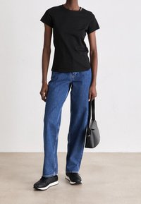 Sort bomulds t-shirt med korte ærmer, parret med blå lige ben jeans. Sorte sneakers med hvide såler, der holder en sort skuldertaske.