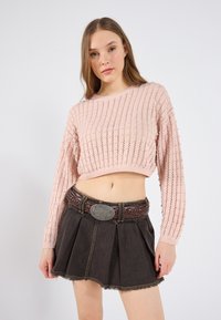 Lys rosa strikket crop genser med et teksturert mønster, parret med en mørk denim plissert miniskjørt og et flettet brunt belte med en sølvspenne.