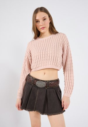 Maglione corto in cotone rosa chiaro con un motivo a trama abbinato a una minigonna plissettata in denim scuro e una cintura intrecciata marrone con una fibbia argento.
