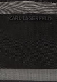Un tessuto nero testurizzato presenta righe grigie orizzontali e un logo nero prominente con la scritta "KARL LAGERFELD" impressa in basso.