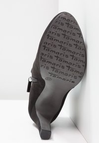 Semelle d'une chaussure à talons haute noire avec un motif texturé du logo "Tamaris" et la taille 37 indiquée au bas.