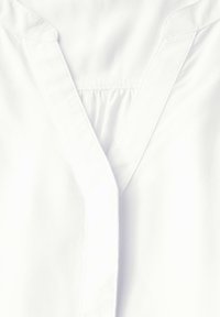 White shirt featuring a v-neck design, soft fabric, subtle texture, and a pleated detail at the neckline. Structured collar with clean lines.