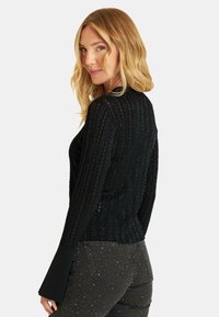 Czarny sweter z żebrowanym splotem, z długimi, rozszerzającymi się rękawami. Teksturowany wzór z delikatnym połyskiem. Dopasowany krój, z widokiem z tyłu.