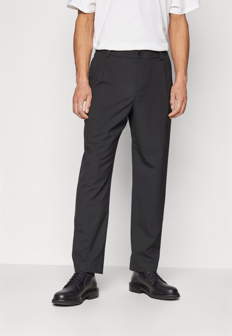 Svarta byxor med avslappnad passform, med knappstängning, sidofickor och elastisk midja. Matchat med svarta läderskor.