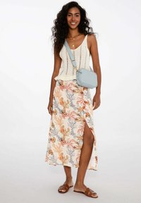 Lehká krémová maxi sukně s květinovým vzorem v oranžové, červené a šedé barvě. Spárovaná s pleteným tílkem a světle modrou crossbody taškou.