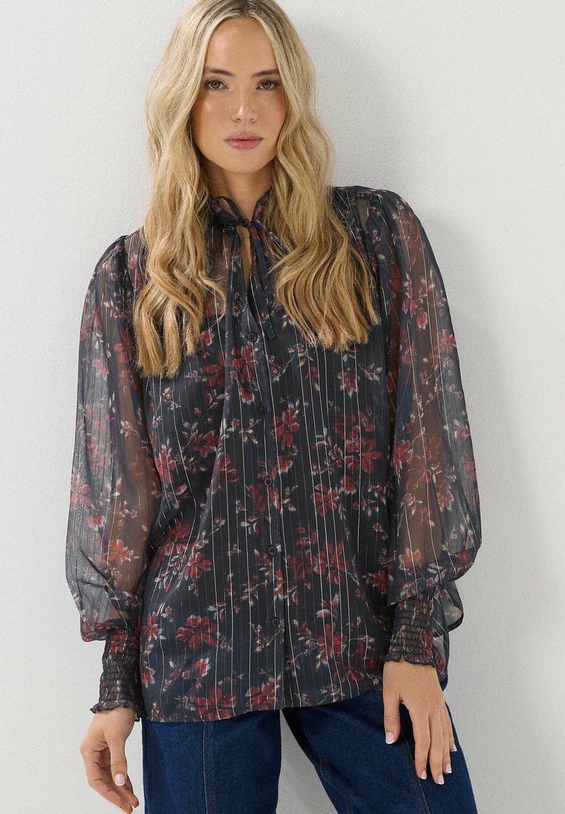 Schwarze, transparente Bluse mit floralen Mustern in Rot und Rosa, mit langen Puffärmeln, Knopfverschluss und einer Krawatte am Hals. Strukturierter, gestreifter Entwurf.