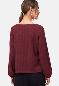 Pull en bourgogne texturé avec des manches longues et un décolleté large, arborant un motif en zigzag et une coupe décontractée.