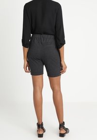 Haut noir à manches longues associé à un short gris foncé. Le short présente une taille élastique et une texture lisse. Des sandales à boucle complètent la tenue.