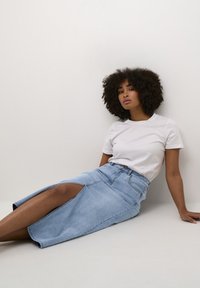 Gonna midi in denim azzurro chiaro con una grande fessura laterale, abbinata a una t-shirt bianca semplice, caratterizzata da una vita aderente e un design casual.