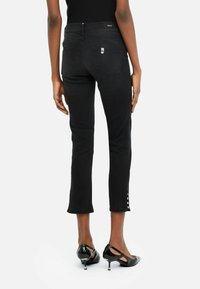 Jean cropped noir avec un design épuré, deux poches arrière et un détail de bouton à l'ourlet. Fabriqué en denim avec une texture lisse.