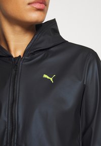 Black hooded jacket made of smooth fabric. Features a zip closure and a small yellow Puma logo on the left chest.